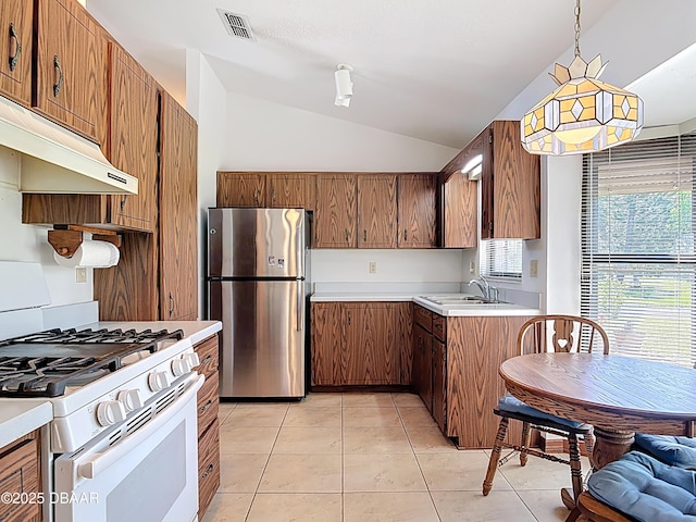 kitchen with white gas stove, light tile patterned flooring, freestanding refrigerator, a sink, and under cabinet range hood