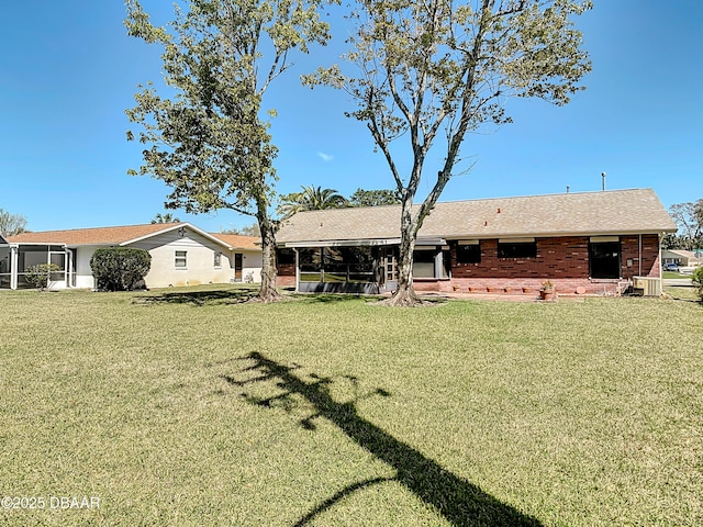 rear view of property with brick siding, central AC, a yard, and a sunroom