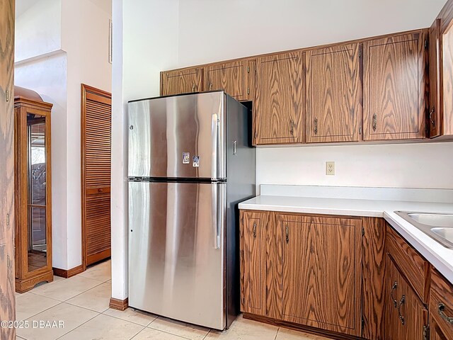 kitchen with light tile patterned flooring, brown cabinets, light countertops, and freestanding refrigerator