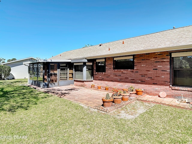 rear view of property featuring a patio, roof with shingles, a sunroom, a lawn, and brick siding