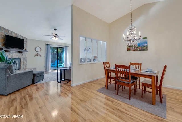 dining room with ceiling fan with notable chandelier, light hardwood / wood-style floors, a stone fireplace, and vaulted ceiling