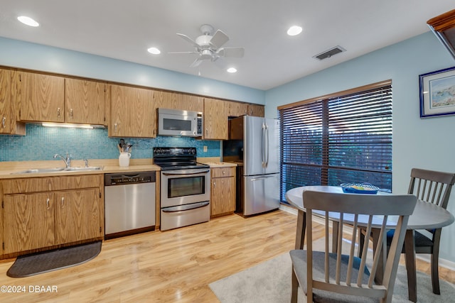 kitchen with appliances with stainless steel finishes, tasteful backsplash, ceiling fan, sink, and light hardwood / wood-style flooring