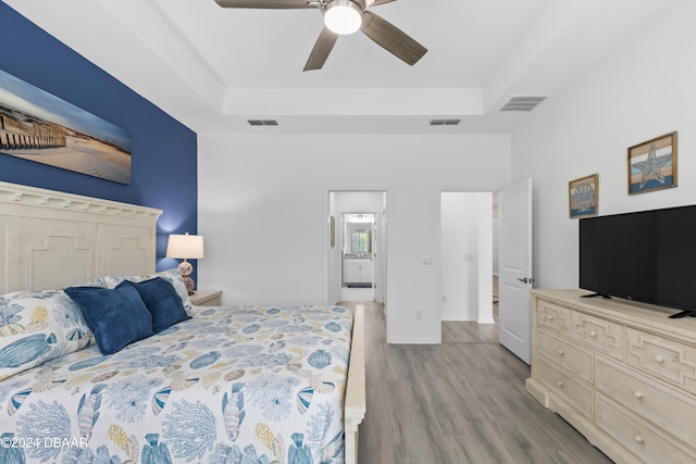 bedroom featuring light hardwood / wood-style floors, ceiling fan, and a raised ceiling