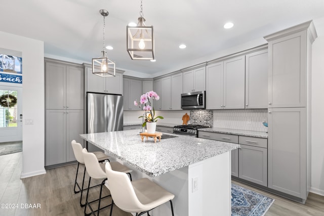 kitchen featuring light stone counters, gray cabinetry, appliances with stainless steel finishes, and an island with sink