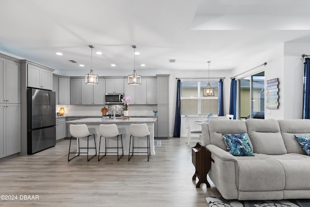 kitchen with light wood-type flooring, appliances with stainless steel finishes, a breakfast bar area, and decorative light fixtures