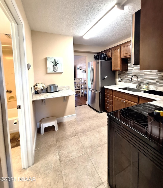 kitchen with sink, a textured ceiling, stainless steel refrigerator, black range with electric cooktop, and decorative backsplash