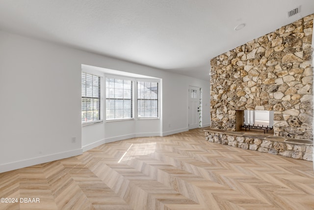 unfurnished living room featuring a stone fireplace, light parquet flooring, and a textured ceiling