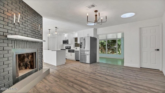 unfurnished living room with sink, hardwood / wood-style floors, a chandelier, and a brick fireplace