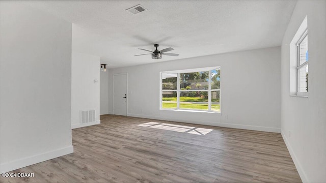 spare room with ceiling fan, a healthy amount of sunlight, a textured ceiling, and light hardwood / wood-style flooring