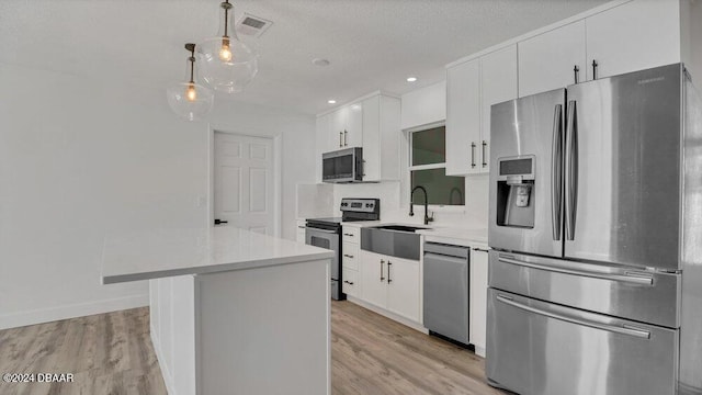 kitchen featuring pendant lighting, white cabinets, light wood-type flooring, a textured ceiling, and appliances with stainless steel finishes