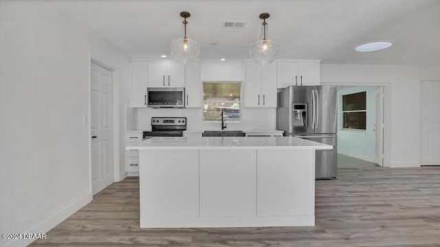 kitchen with appliances with stainless steel finishes, a kitchen island, sink, decorative light fixtures, and white cabinetry