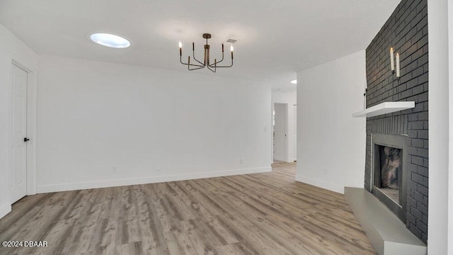 unfurnished living room featuring a chandelier, light hardwood / wood-style floors, and a brick fireplace