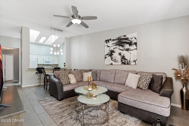 living room with ceiling fan, lofted ceiling with skylight, tile patterned flooring, and a textured ceiling