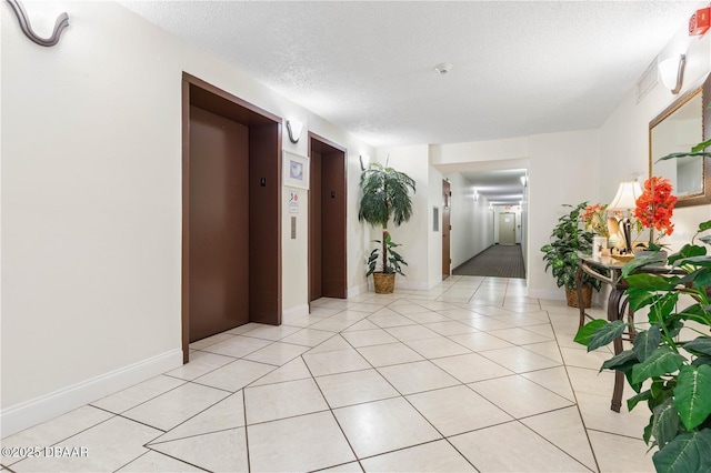 hall with light tile patterned floors, a textured ceiling, and elevator