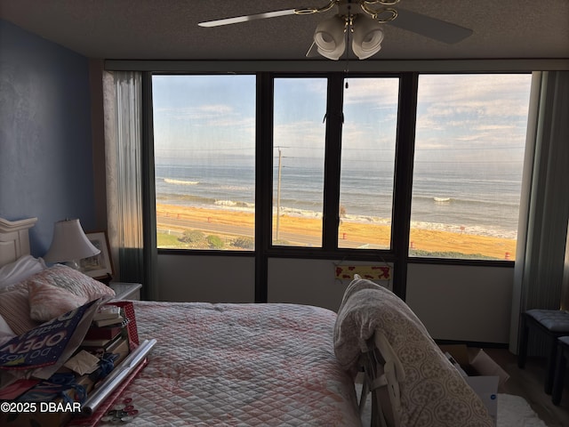 bedroom featuring ceiling fan, a textured ceiling, a beach view, and a water view