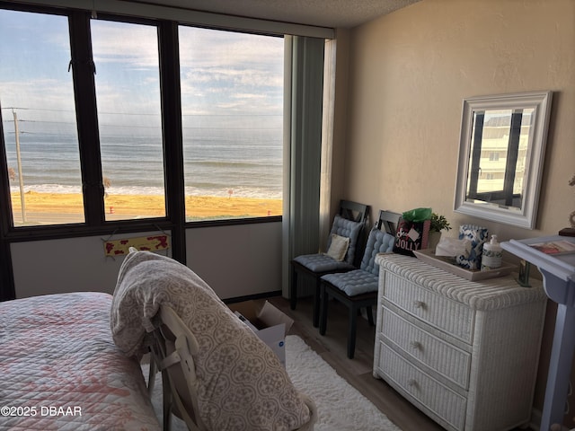 bedroom with multiple windows, hardwood / wood-style floors, a beach view, and a water view