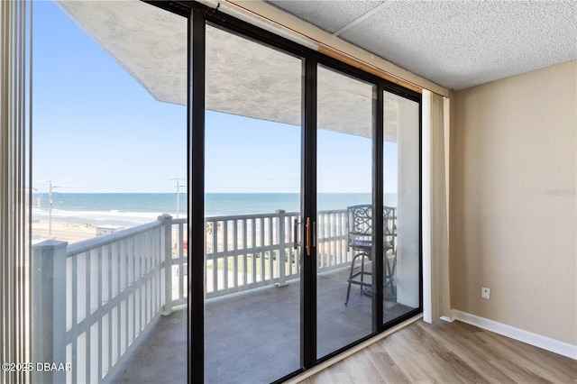 doorway with a water view, a beach view, floor to ceiling windows, and light wood-type flooring