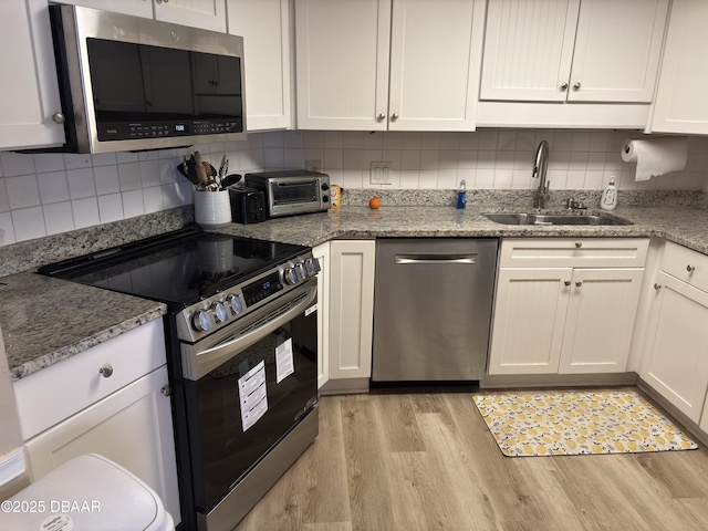 3580 S Ocean Shore Blvd Unit 404, Flagler Beach, FL 32136 - kitchen with appliances with stainless steel finishes, a sink, light wood-style floors, white cabinets, and tasteful backsplash