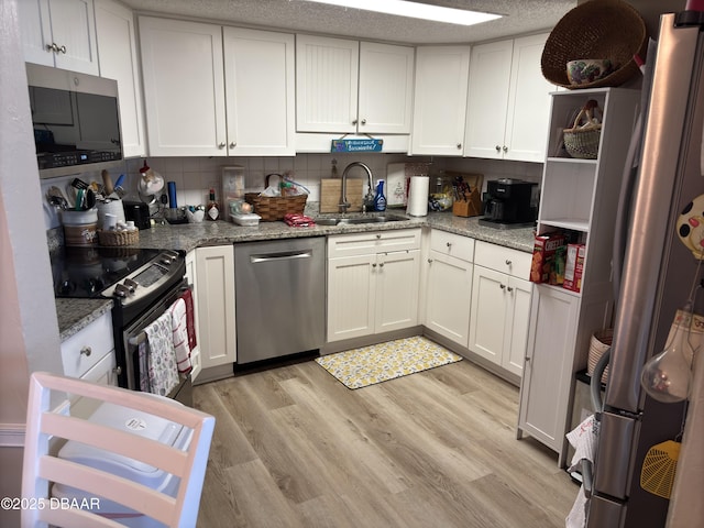 kitchen featuring sink, appliances with stainless steel finishes, light stone counters, light hardwood / wood-style floors, and white cabinets