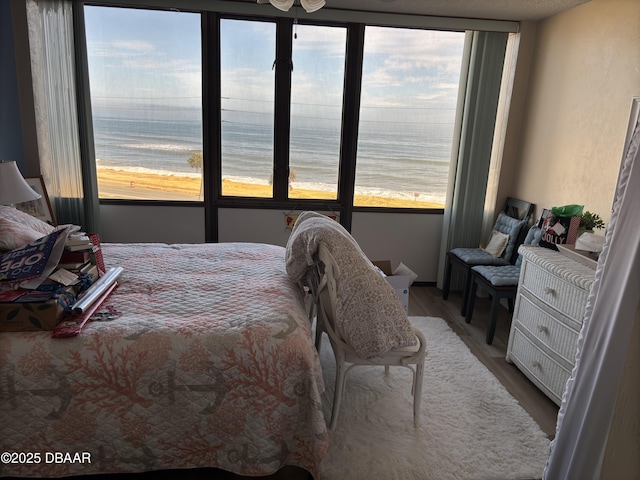 bedroom with multiple windows, wood-type flooring, a water view, and a view of the beach