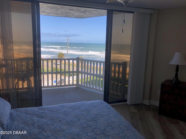 bedroom with wood-type flooring, a water view, and a beach view