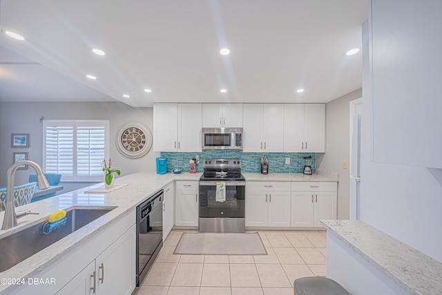 kitchen with stainless steel appliances, sink, light tile patterned floors, light stone countertops, and white cabinetry