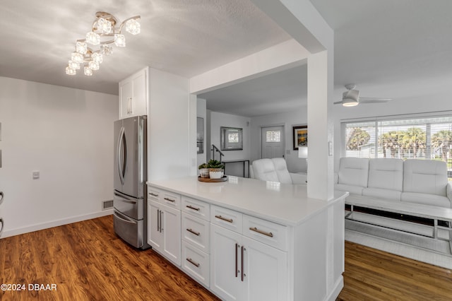 kitchen featuring ceiling fan with notable chandelier, dark wood-type flooring, kitchen peninsula, stainless steel refrigerator, and white cabinetry