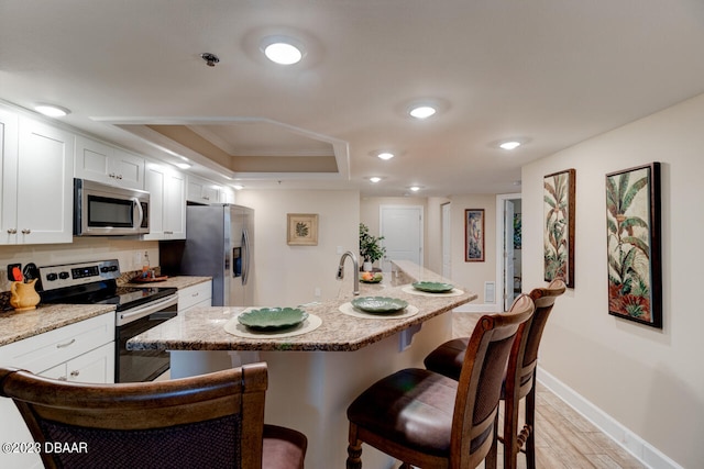 kitchen with stainless steel appliances, a center island with sink, a breakfast bar, light stone counters, and white cabinets