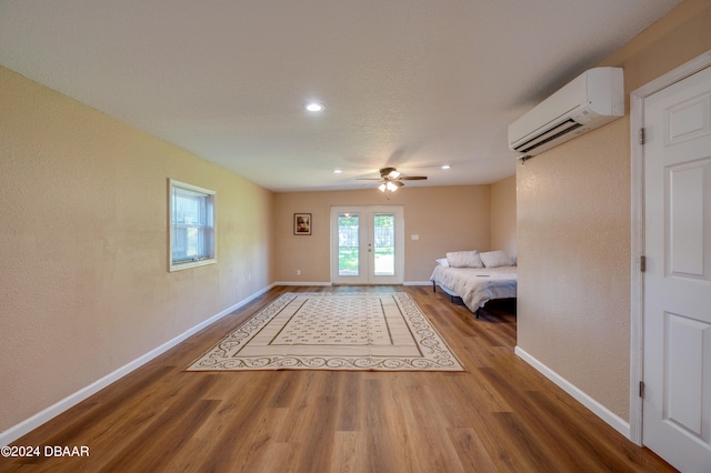 unfurnished bedroom with ceiling fan, a wall unit AC, wood-type flooring, and french doors