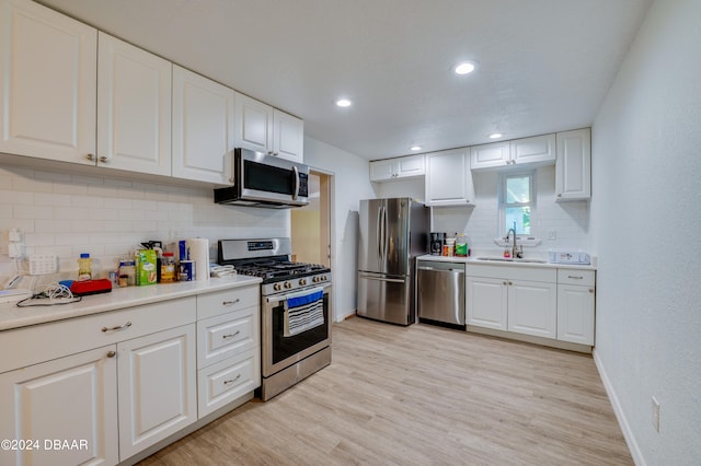 kitchen featuring stainless steel appliances, light hardwood / wood-style floors, white cabinets, sink, and tasteful backsplash