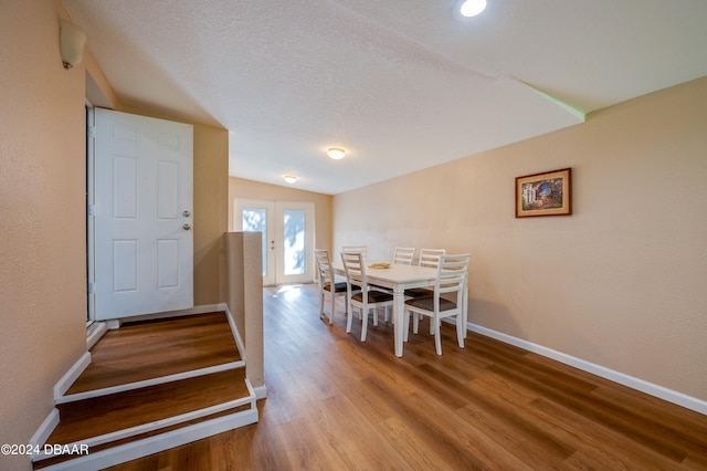 dining room featuring wood-type flooring, a textured ceiling, and vaulted ceiling