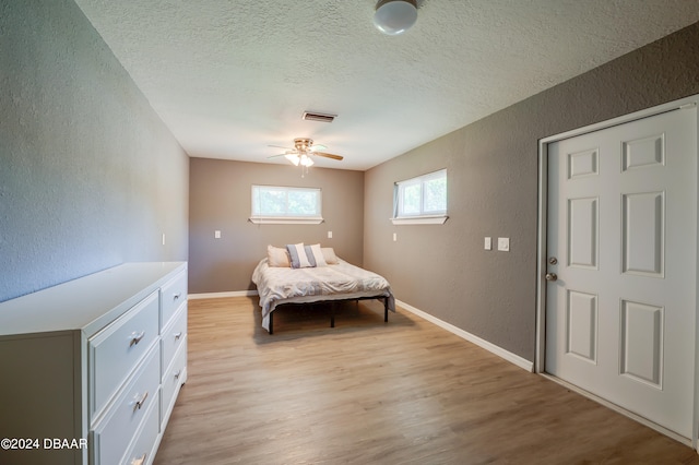 bedroom with ceiling fan, a textured ceiling, and light hardwood / wood-style floors