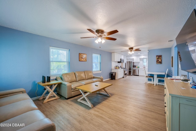 living room with ceiling fan, a textured ceiling, and light wood-type flooring