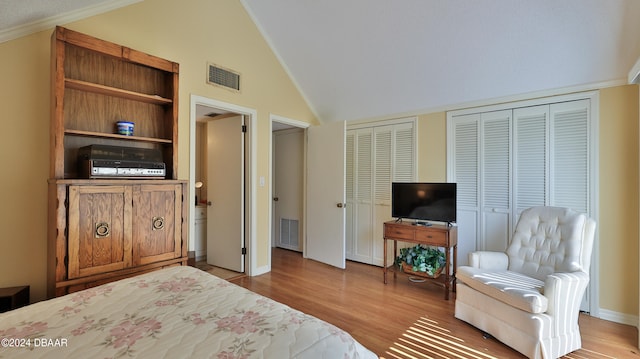 bedroom featuring light hardwood / wood-style floors, lofted ceiling, crown molding, and two closets