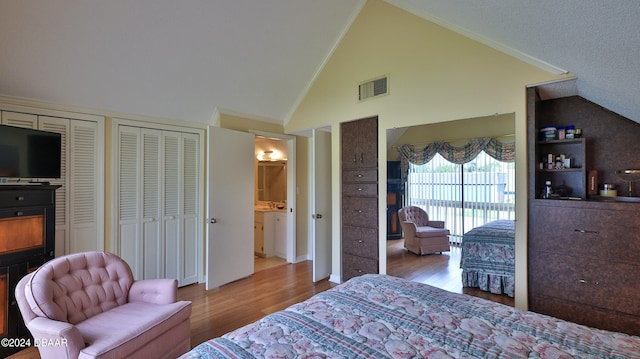 bedroom with two closets, light wood-type flooring, vaulted ceiling, and ornamental molding