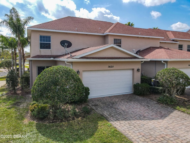 traditional-style house with stucco siding, a garage, roof with shingles, and driveway