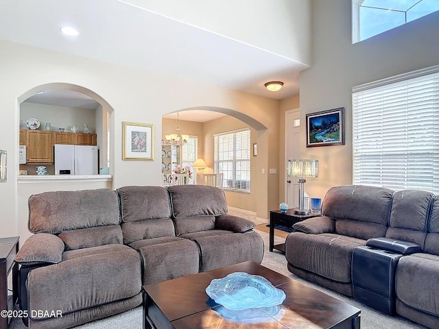 carpeted living area with a wealth of natural light, baseboards, arched walkways, and a notable chandelier