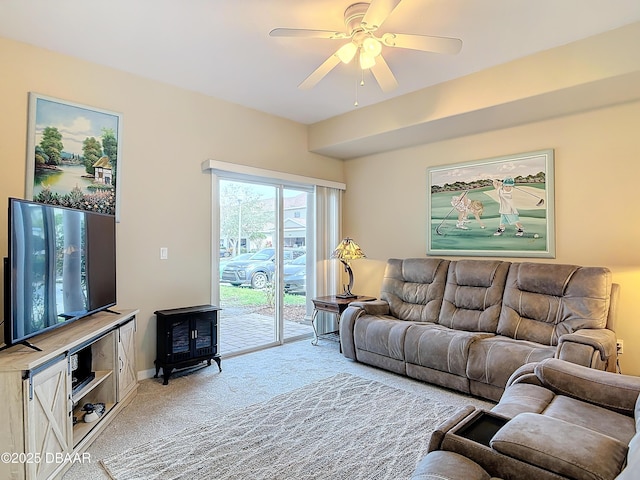 living area featuring a wood stove, light colored carpet, baseboards, and ceiling fan