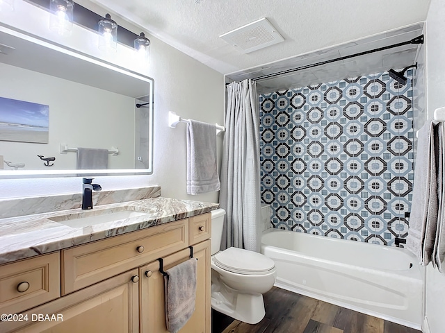 full bathroom with a textured ceiling, shower / bathtub combination with curtain, hardwood / wood-style floors, vanity, and toilet