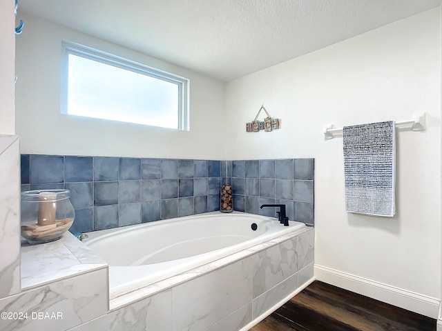 bathroom with tiled bath, a textured ceiling, and hardwood / wood-style flooring