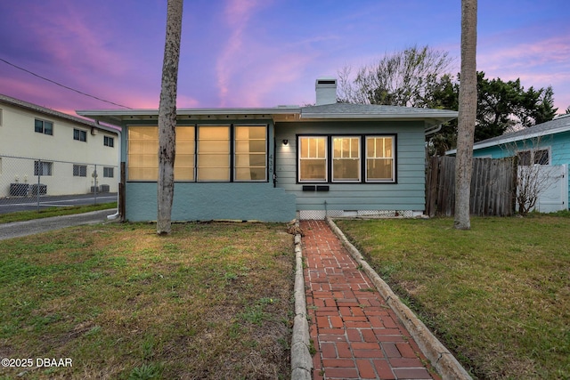 view of front of home featuring fence, a chimney, and a front lawn