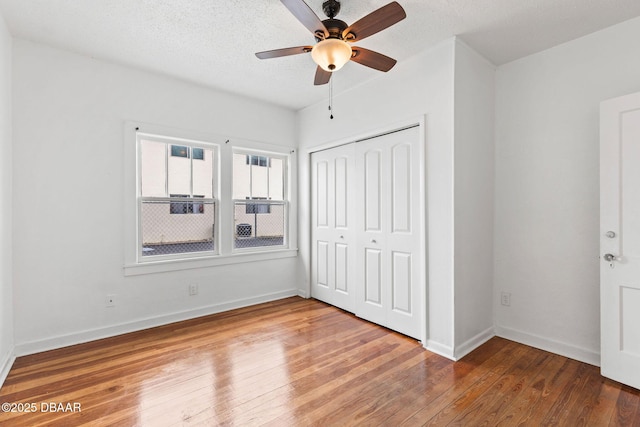 unfurnished bedroom featuring a closet, wood-type flooring, ceiling fan, a textured ceiling, and baseboards