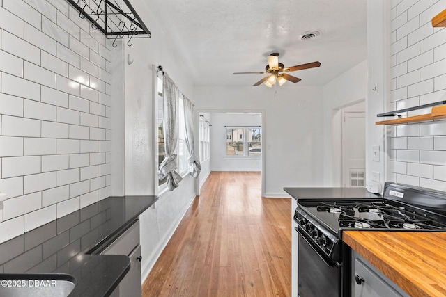 kitchen with black range with gas cooktop, visible vents, wooden counters, backsplash, and light wood finished floors