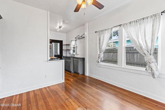 unfurnished living room with wood finished floors, visible vents, a sink, a ceiling fan, and baseboards