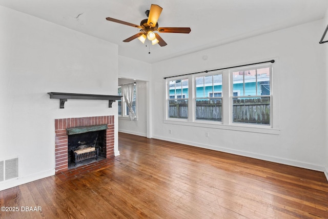 unfurnished living room with a brick fireplace, wood-type flooring, visible vents, and baseboards