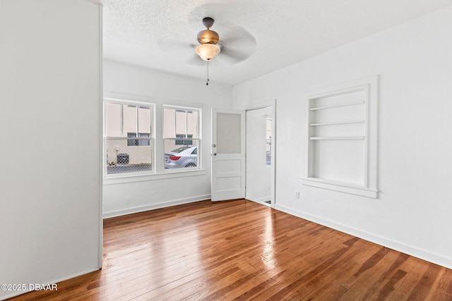 unfurnished room featuring a textured ceiling, ceiling fan, baseboards, built in features, and hardwood / wood-style floors