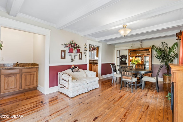 living room featuring beam ceiling, light hardwood / wood-style flooring, ornamental molding, and sink