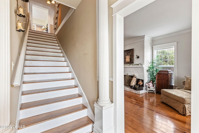 stairs with ornate columns, a brick fireplace, ornamental molding, and hardwood / wood-style flooring