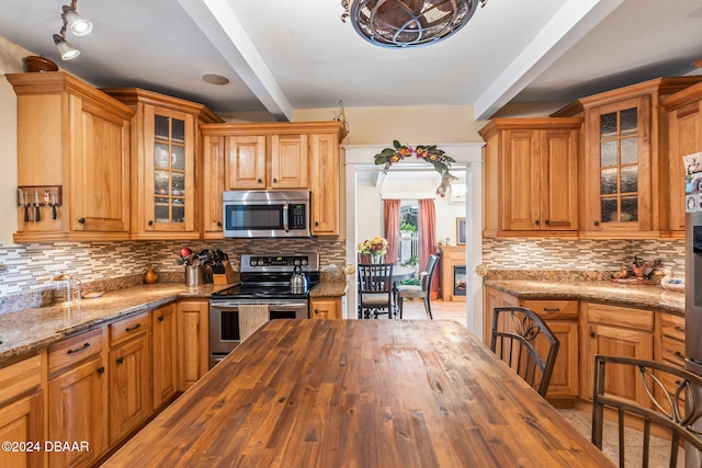 kitchen with tasteful backsplash, butcher block counters, beamed ceiling, and appliances with stainless steel finishes