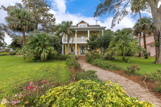 beach home with covered porch, a balcony, and a front lawn